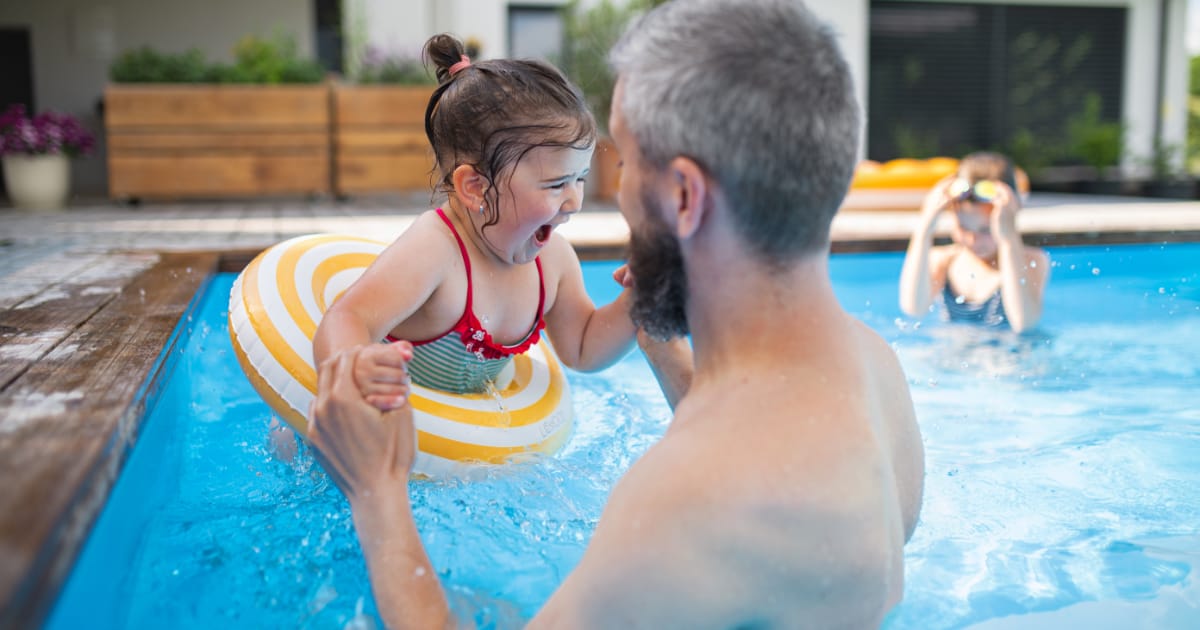 Father and daughter playing Father with happy daughter outdoors in the backyard, playing in swimming pool.